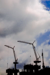 Low angle view of cranes at construction site against sky