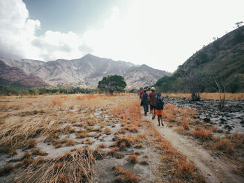 Rear view of men walking on field against mountains