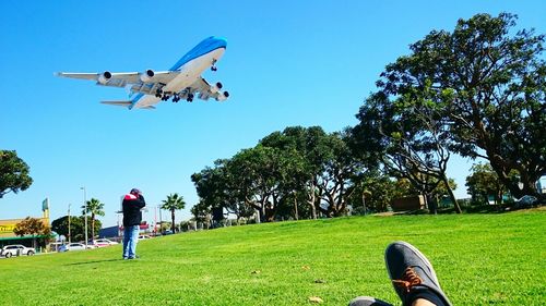 Man standing on field while airplane flying in sky