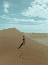 Man on sand dune in desert against sky