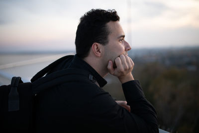 Side view of thoughtful man with hand on chin looking away against sky