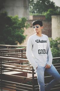 Young man wearing sunglasses standing by railing outdoors