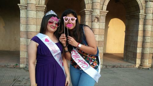 Portrait of smiling females with props while standing against building