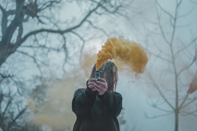 Close-up of man holding bare tree against sky