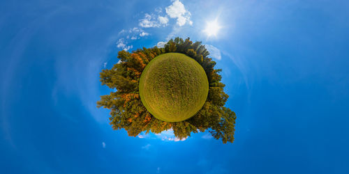 Little planet projection panorama of sunny autumnal meadow, yellow forest with blue sky and clouds