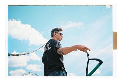 Side view of young man holding camera against sky