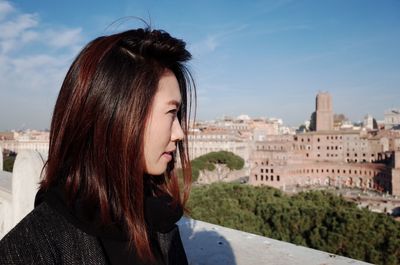 Woman with brown hair on building terrace against sky in city