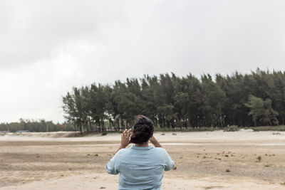 Rear view of woman standing at beach against sky