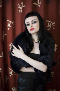 Portrait of young woman standing against curtain