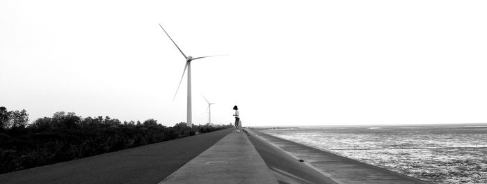 Low angle view of wind turbines on road against clear sky