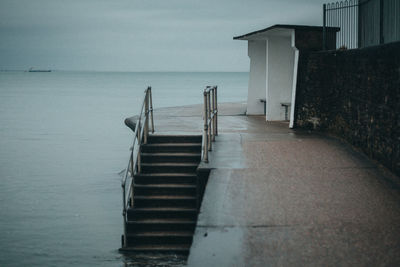 Empty deck chairs by sea against sky