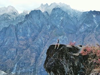 Low angle view of man sitting on cliff against mountains at tiger leaping gorge