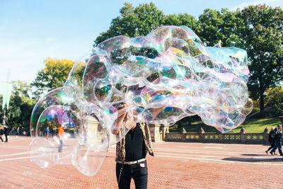 Full length of man with bubbles in park against sky
