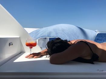 Woman with drink lying down on boat at beach against sky