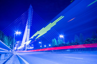 Light trails on road against blue sky at night