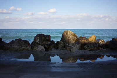 Rock formations at sea shore against sky