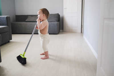 Toddler 1 year old with broom sweeps floor in bright room 