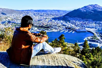 Man sitting on rock against sky