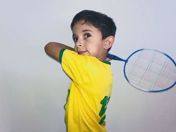 Thoughtful boy holding badminton racket against white background