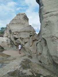 Full length side view of young woman walking at beach by rock formation