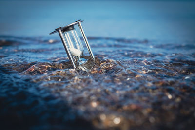 An hourglass is stuck in the shore sand of the sea and is washed around by the water