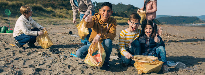 Young man and children posing while picking up trash with group of volunteers on the beach