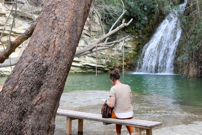 Rear view of young woman sitting on bench by lake