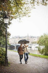 Young couple with umbrella walking on street during autumn