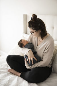 Hipster millenial mom smiles down at swaddled newborn son