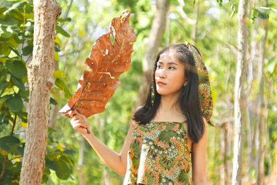 Young woman looking away while standing on tree