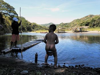Rear view of shirtless man standing on lake against sky