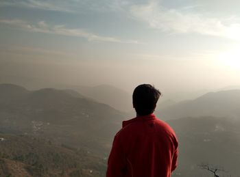 Rear view of man looking at mountains during foggy weather