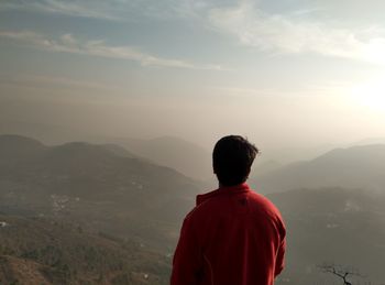 Rear view of man looking at mountains against sky