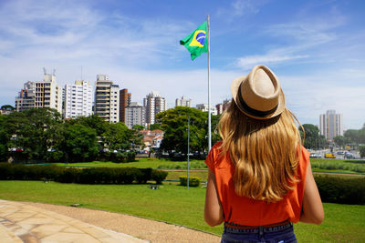 Brazilian girl looking the national flag with sao paulo cityscape on the background, brazil