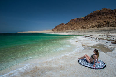 Woman sitting on beach against clear sky