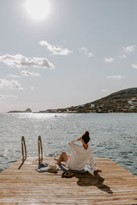 Rear view of woman sitting on pier by sea