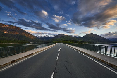 Empty road leading towards mountains against sky