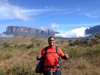 Portrait of man showing thumbs up while standing on field against mountains at kukenan-tepui