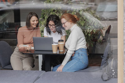 Smiling woman using laptop sitting by friends at cafe