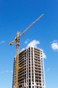 Low angle view of crane by building against sky