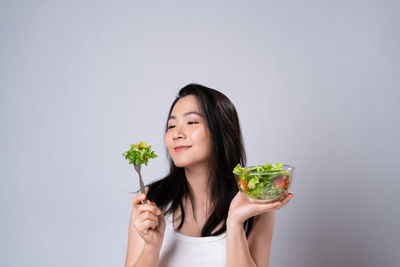 Portrait of a smiling young woman holding ice cream against white background