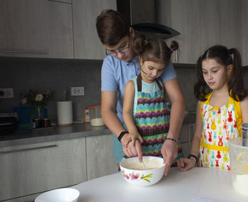 Friendly sisters and brother baking traditional  cookies on the domestic kitchen