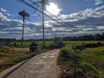 Road amidst trees on field against sky