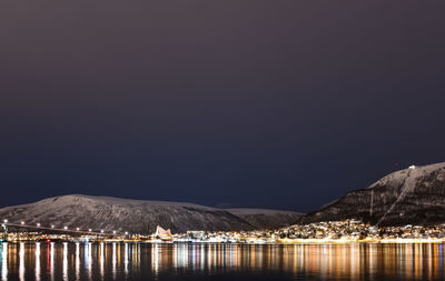 Scenic view of lake by illuminated mountains against clear sky at night