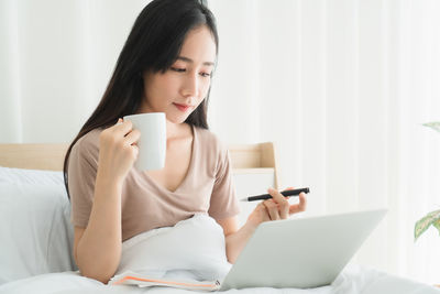 Young woman using phone while sitting on laptop