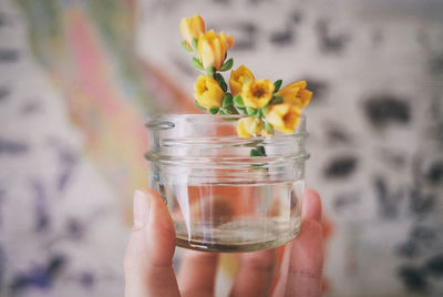 Cropped hand holding yellow flowers in glass container