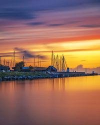 Sailboats moored in sea against sky during sunset