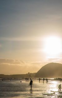 Silhouette people on low tide beach against sky during sunset with a surfer prominent