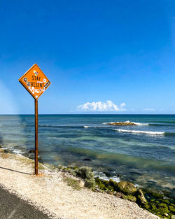 Information sign on beach against blue sky