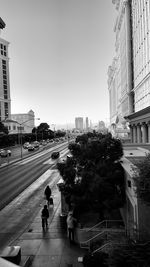 People on city street by buildings against clear sky